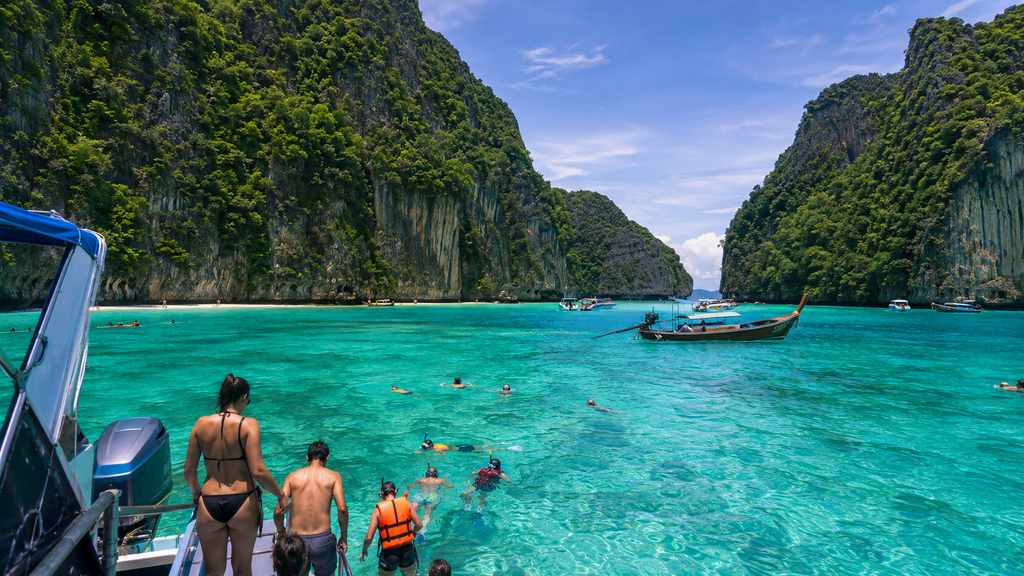 Travelers swimming and snorkeling in turquoise water surrounded by limestone cliffs near Phuket